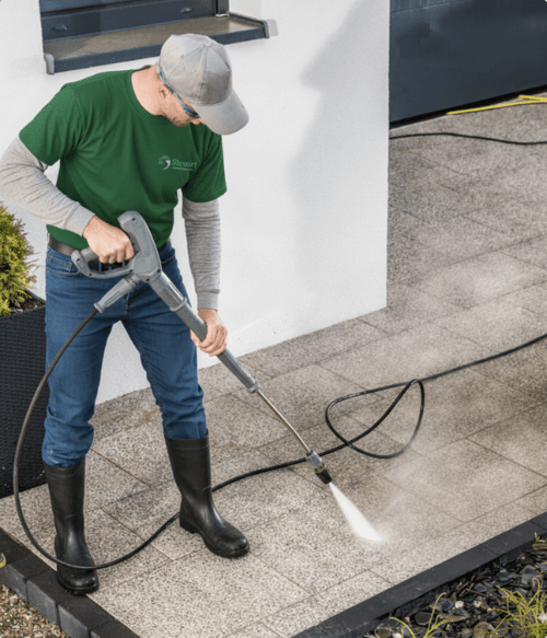 A Stewart Grounds Management Employee pressure washing a residential homes patio.